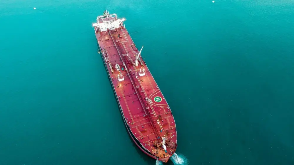 Aerial view of a large red oil tanker cruising through teal water