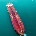 Aerial view of a large red oil tanker cruising through teal water