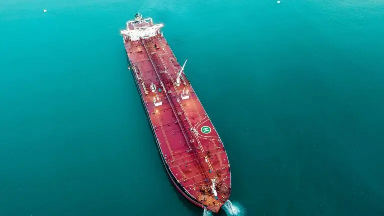 Aerial view of a large red oil tanker cruising through teal water