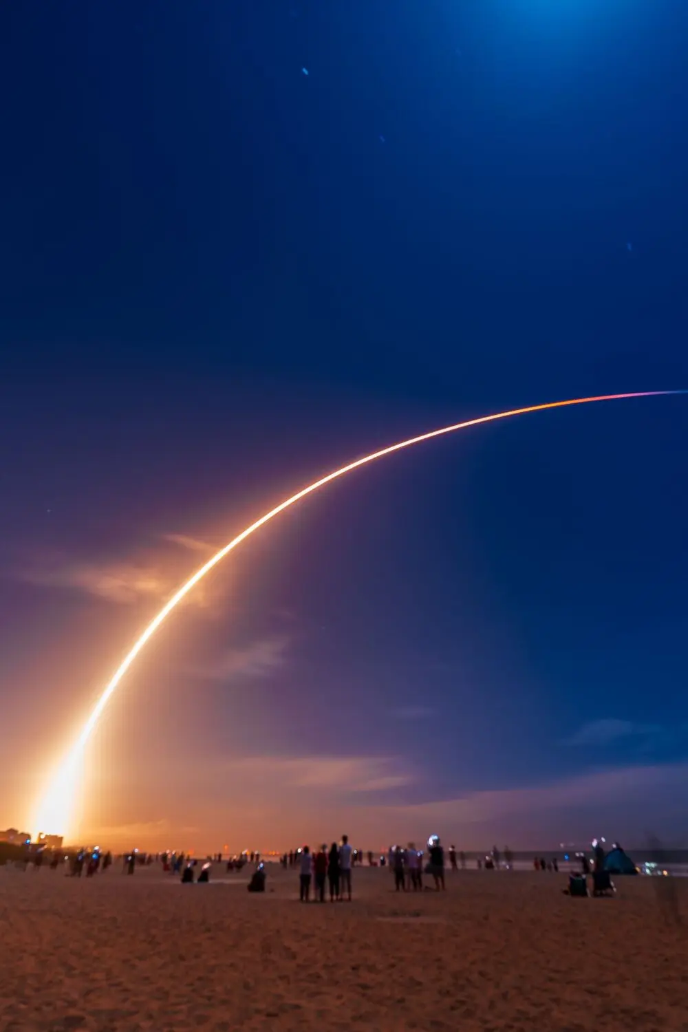 A rocket launch leaving a bright arc of light across a deep blue sky