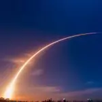 A rocket launch leaving a bright arc of light across a deep blue sky