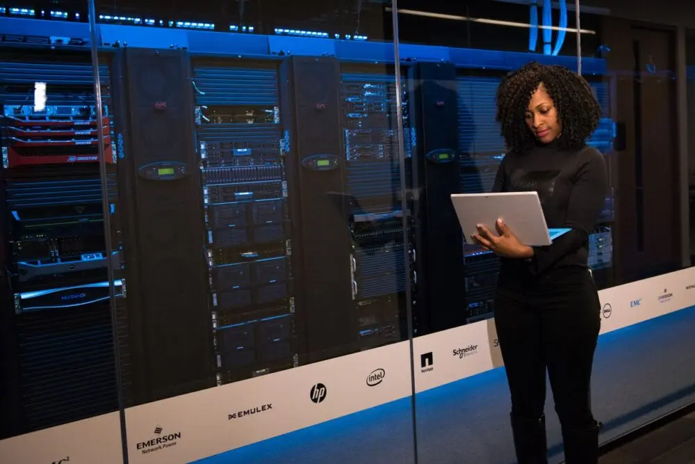 Engineer with a laptop standing beside data center server racks