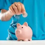 Hand dropping a coin into a piggy bank, illustrating the 2027 401(k) limit