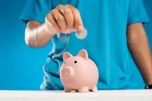 Hand dropping a coin into a piggy bank, illustrating the 2027 401(k) limit