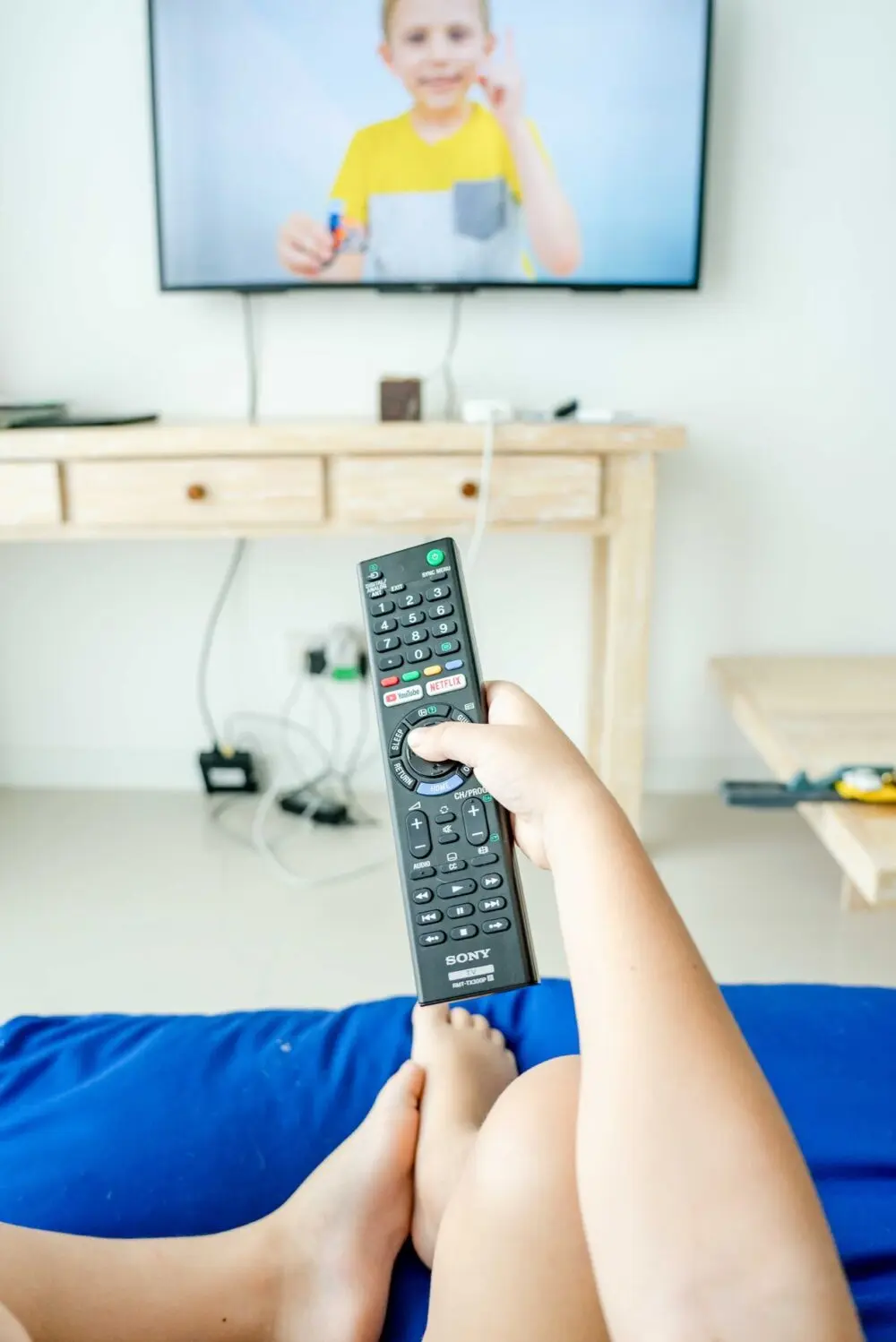 Hand holding a TV remote pointed at a screen, illustrating Netflix earnings preview viewing habits