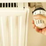 Hand turning a radiator thermostat dial to manage winter heating costs