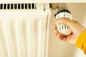 Hand turning a radiator thermostat dial to manage winter heating costs