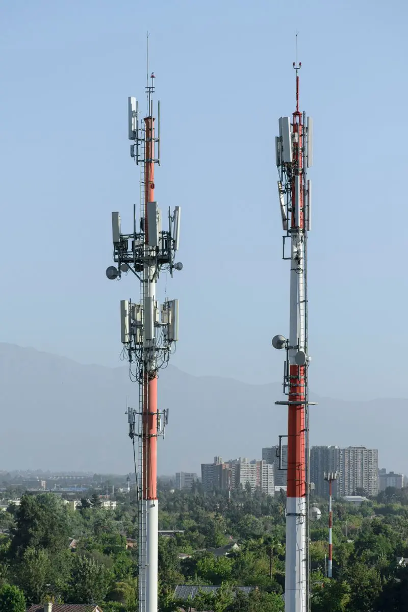 Two cell towers with antennas rising above a city skyline, the ground network Starlink Mobile aims to rival