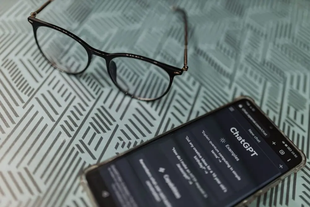 Smartphone with the ChatGPT app next to eyeglasses, illustrating ChatGPT ads targeting