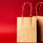 Two brown paper shopping bags with twisted red handles against a red background