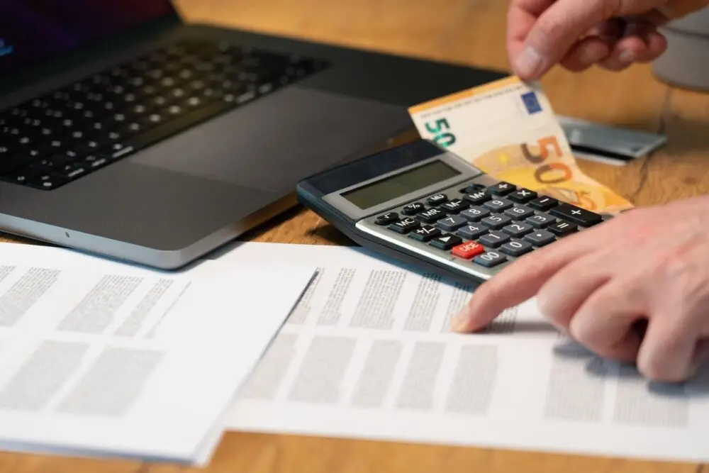 Hands using a calculator over documents and a laptop, representing the CoreWeave credit math