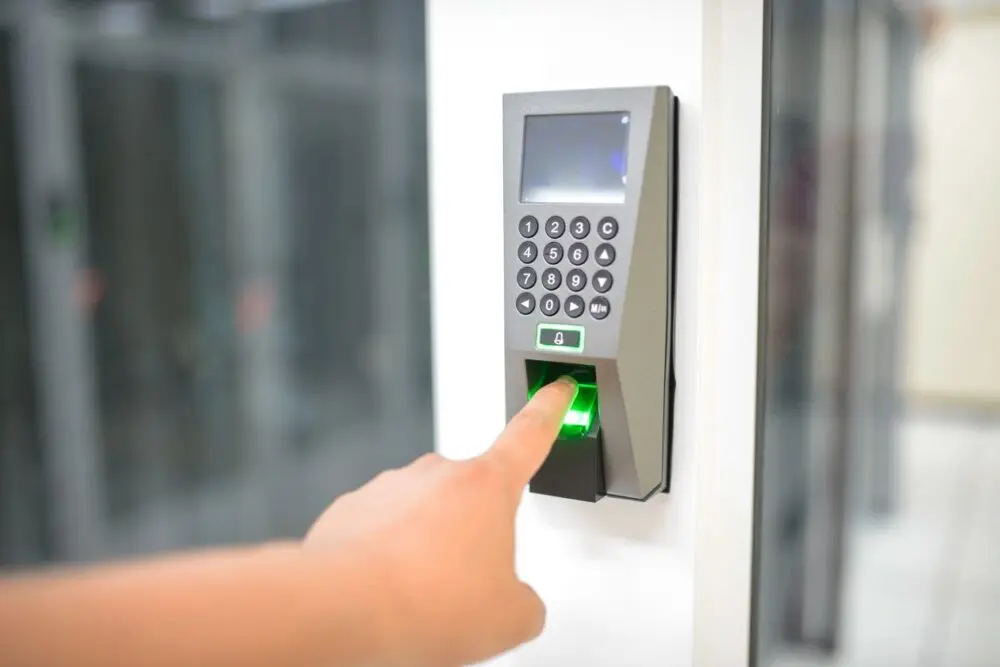Finger on a fingerprint scanner next to a keypad on a wall