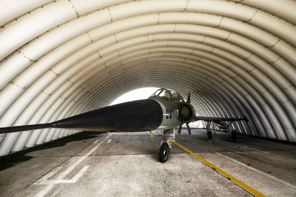 Military aircraft parked inside an arched hangar