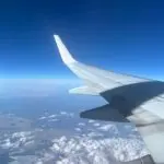 Airplane wing and winglet above clouds against a deep blue sky