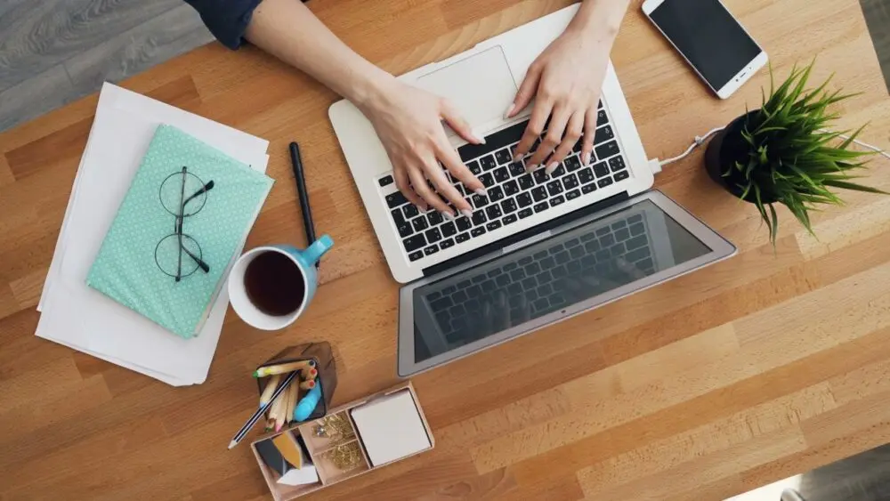 Desk with laptop, notebook and coffee where someone drafts AI prompts
