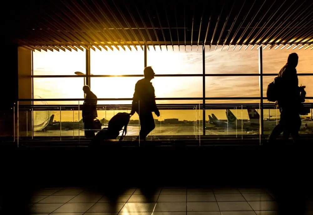 Silhouettes of travelers waiting at an airport window at sunset