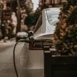 A white electric car plugged in to charge on a city street