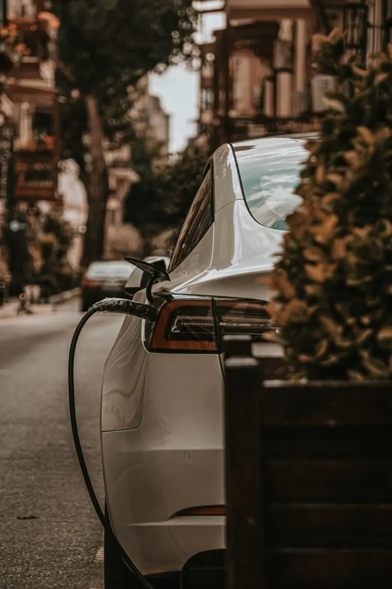 A white electric car plugged in to charge on a city street
