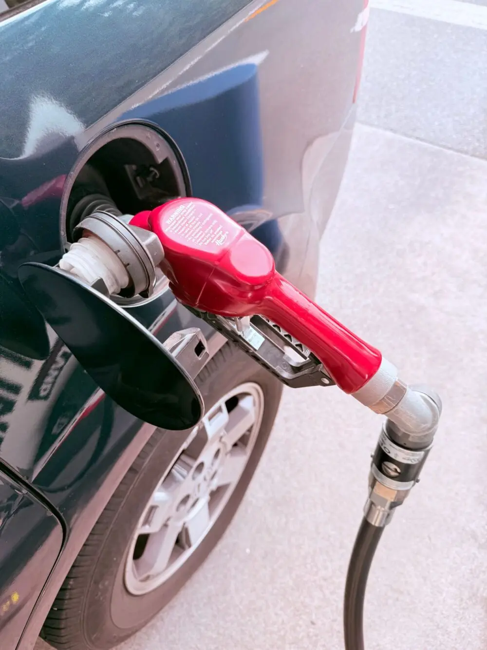 Red gas pump nozzle fueling a car, showing what the Brent crude price means at the pump