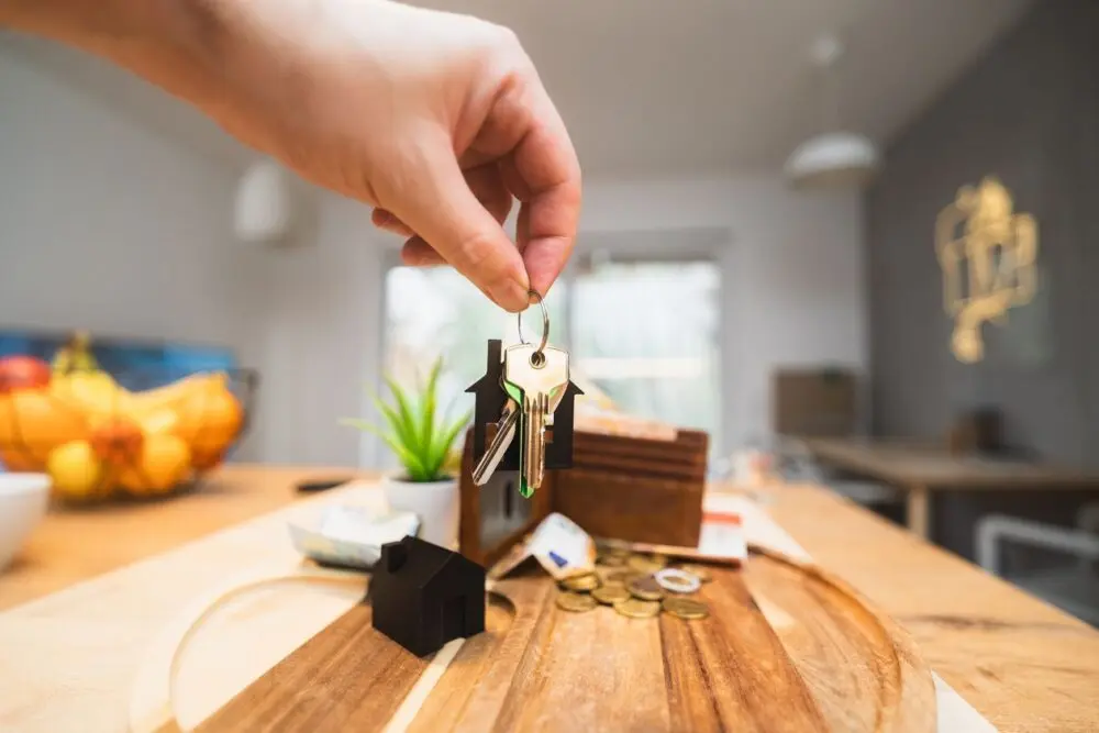 Hand holding house keys over a wooden table in a modern kitchen