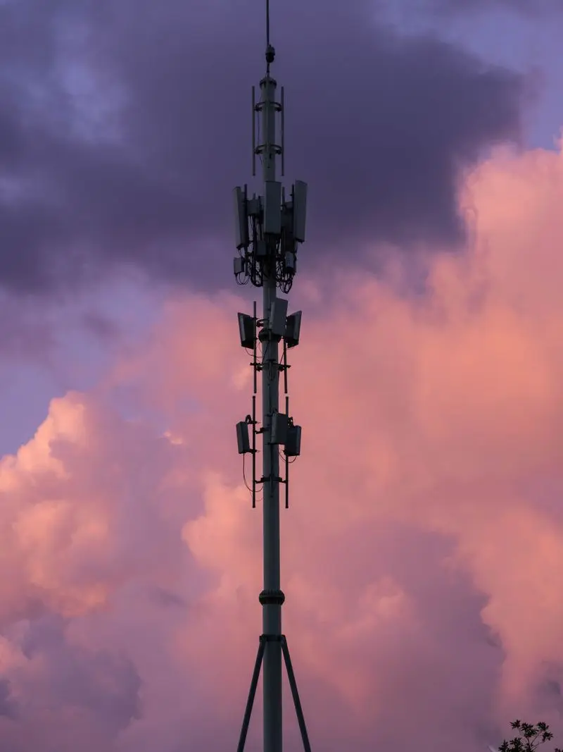 Cell tower silhouetted against a pink and purple evening sky