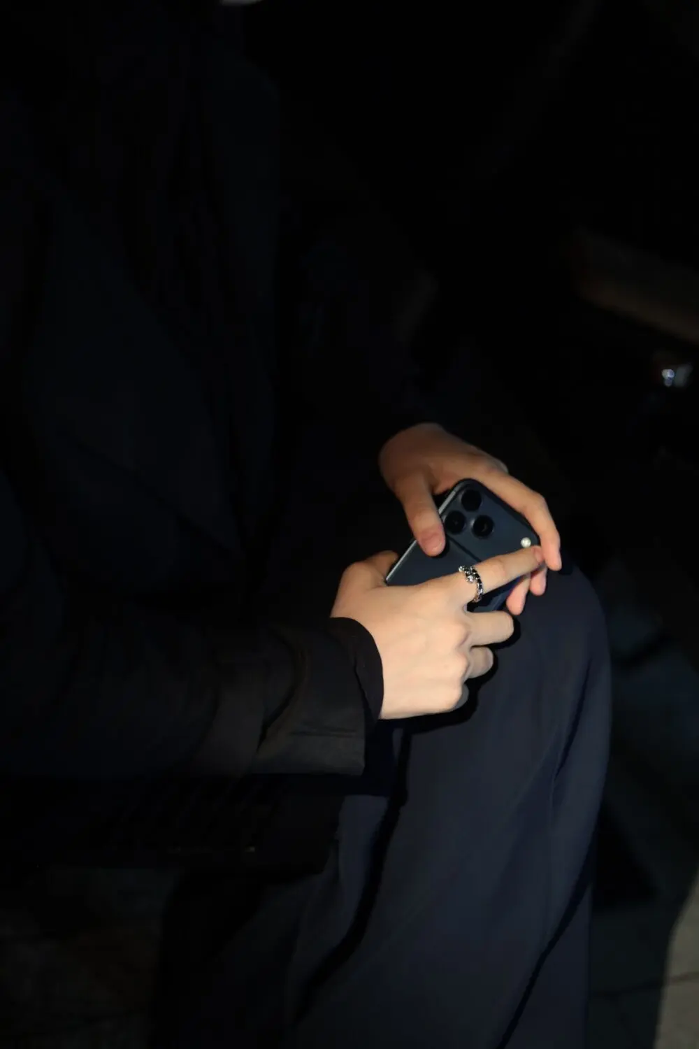 A person holding a smartphone in dim light, illustrating the unexpected calls in a phone number scam