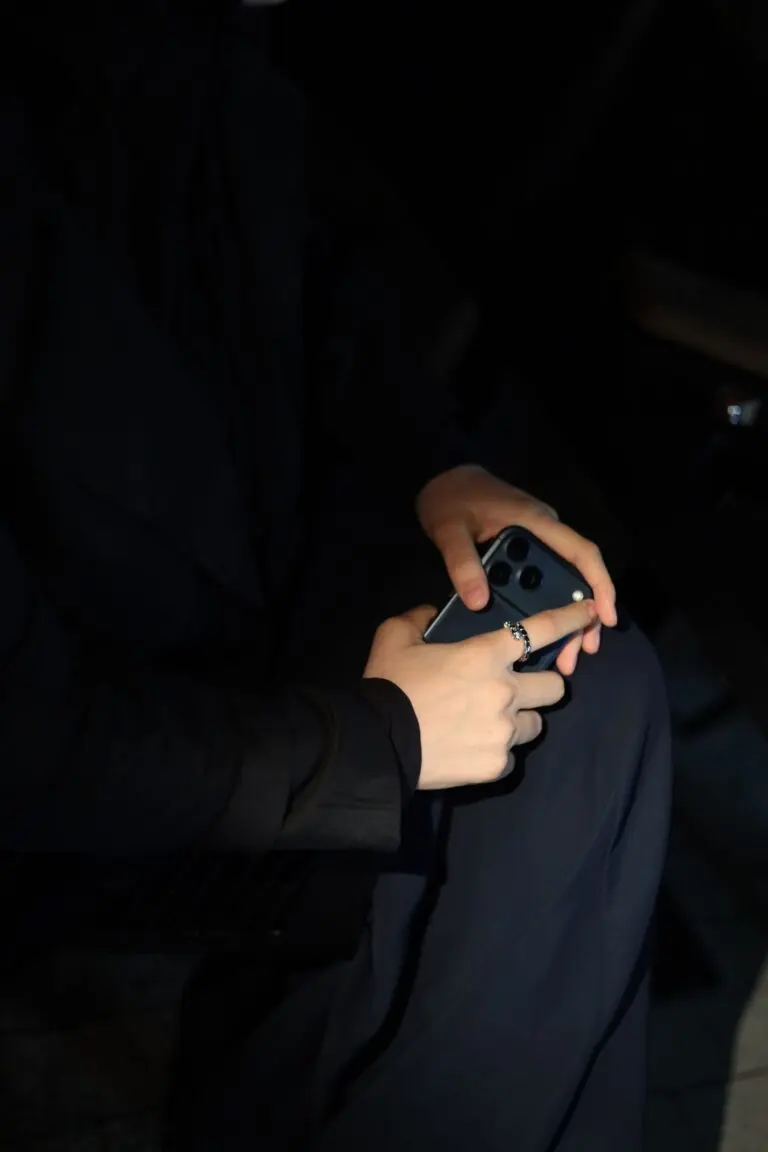 A person holding a smartphone in dim light, illustrating the unexpected calls in a phone number scam