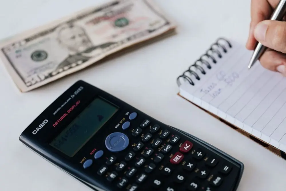 Calculator, banknote and spiral notebook used for monthly budget tracking