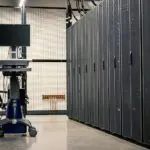 Rows of dark server cabinets in a data center aisle with a monitor on a rolling cart