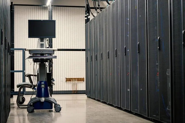 Rows of dark server cabinets in a data center aisle with a monitor on a rolling cart