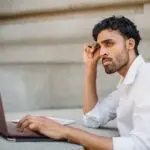 Man in a white shirt working on a laptop at a table, reading initial jobless claims news