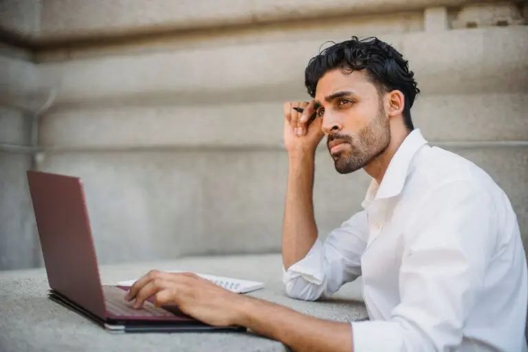Man in a white shirt working on a laptop at a table, reading initial jobless claims news