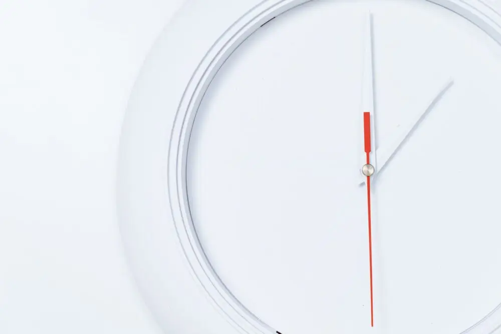 White wall clock with a red second hand, a reminder that daylight saving time ends November 1