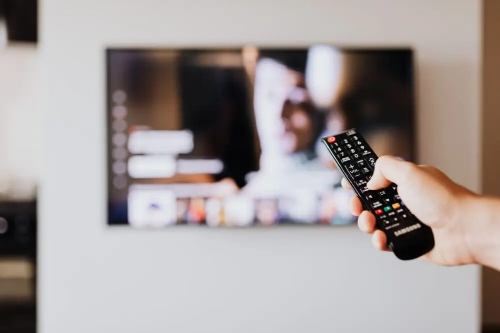 Person using a TV remote control in a living room, the audience behind the Netflix Q3 earnings growth numbers