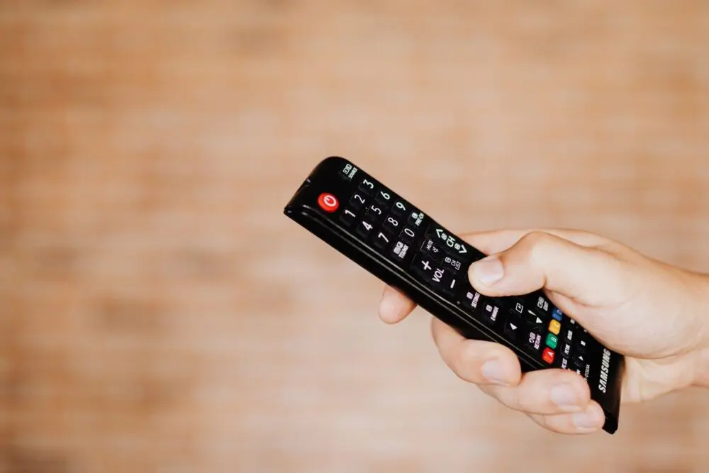 Hand pointing a black remote control at a television