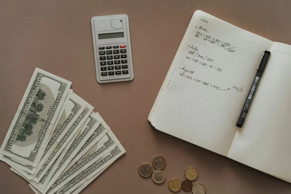 Notebook with a pen, a small calculator and cash laid out on a table