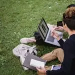Two students study on a laptop outdoors, like many SAVE plan borrowers weighing repayment options