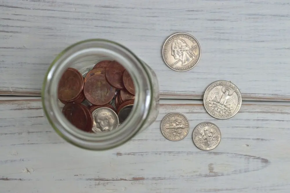Coins in a glass jar on a white wooden table, representing an emergency fund