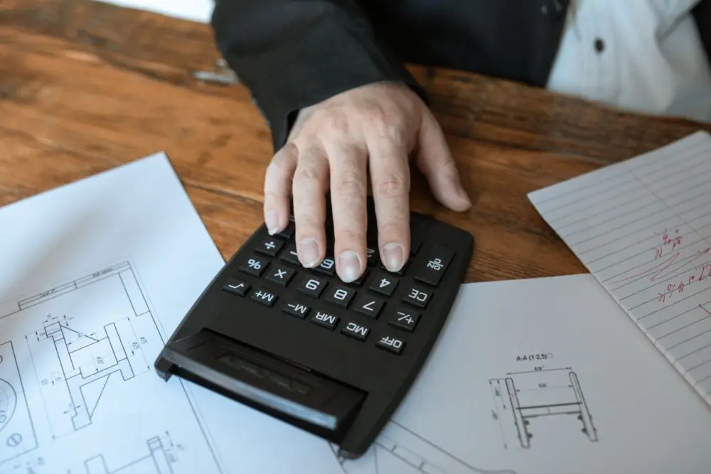 A hand on a calculator beside paperwork while checking costs for ACA open enrollment