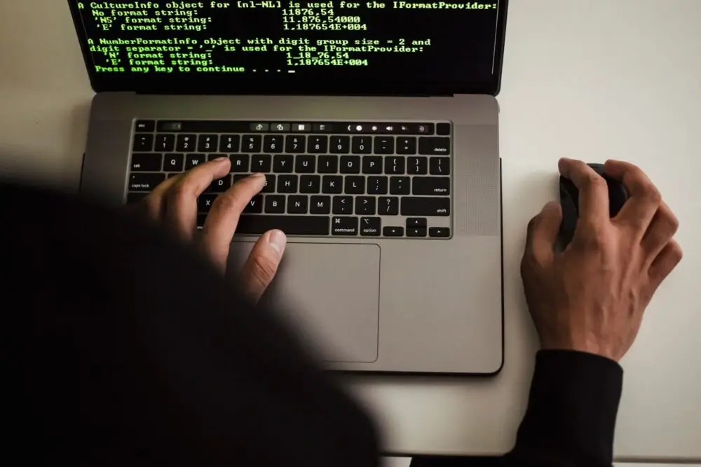 Hands typing on a laptop showing code in a dark room
