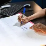 Person writing dates on a paper calendar for a November 2026 money calendar
