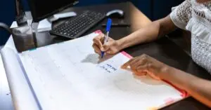 Person writing dates on a paper calendar for a November 2026 money calendar