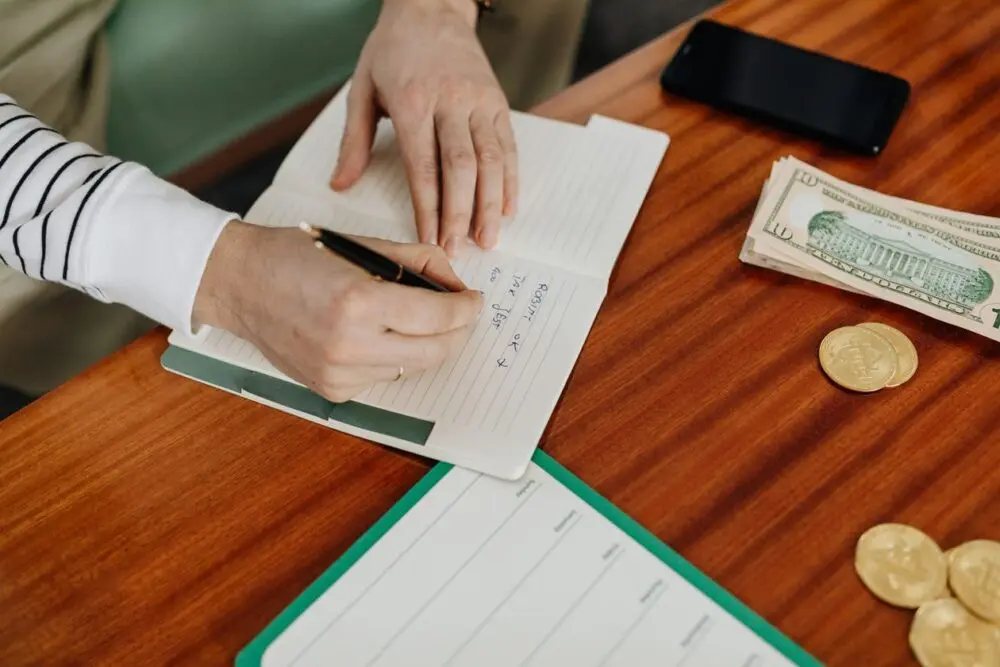 Hand writing numbers in a notebook while working out how to make a budget
