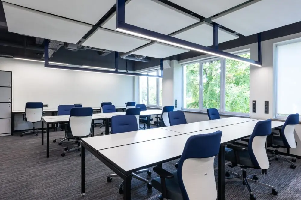 A quiet open-plan office with long desks and blue chairs after October layoffs