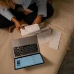 Overhead view of a woman holding a check and a laptop while searching for unclaimed property