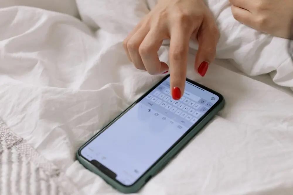 Woman's hand tapping a phone screen to block a scam text sender
