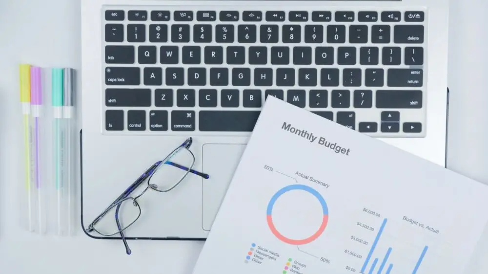 Laptop, budget report and eyeglasses on a desk for planning student loan payments