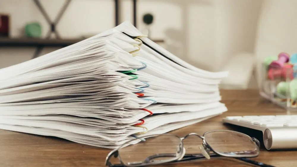Stack of policy paperwork and reading glasses, the kind of documents AI liability insurance exclusions appear in