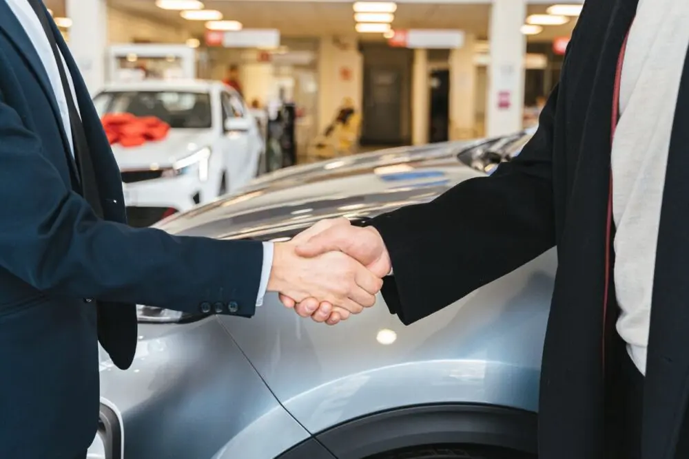 Two people shaking hands next to a car in a showroom