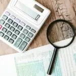 Calculator and magnifying glass beside tax forms for year end tax moves